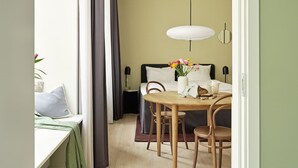Um quarto aconchegante com uma cama, uma mesa de jantar com cadeiras, um vaso de flores e um lustre.