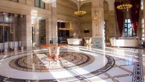 Un vestíbulo espacioso con un diseño circular en el suelo, grandes candelabros y una imponente escalera.