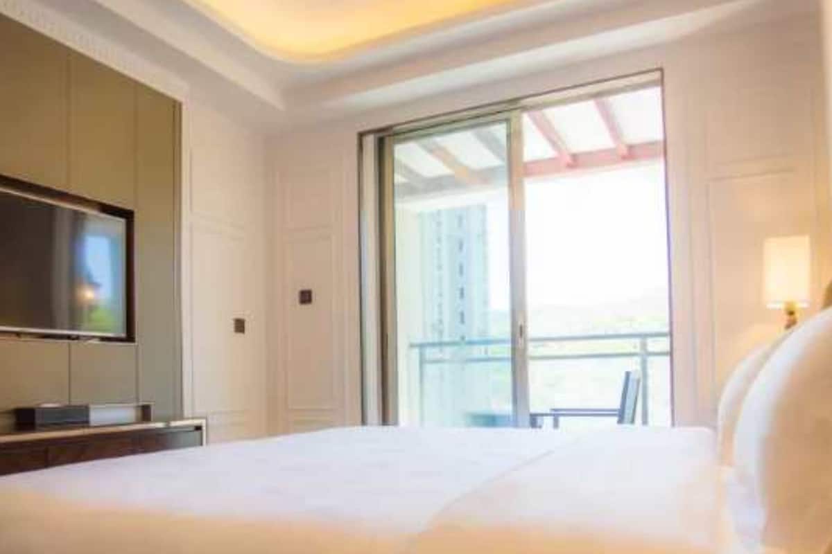 A hotel room with a large bed, a flat-screen TV mounted on the wall, and a balcony with a view.