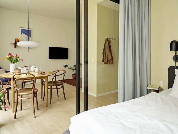 Et hotelværelse med seng, skrivebord med stole, fjernsyn og et badeværelse, der kan ses igennem en åben dør.