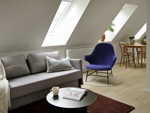 A modern loft apartment with a grey sofa, a blue armchair, and a dining table with wooden chairs. - Attic Studio Apartment for 2 (København)