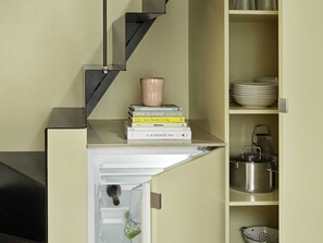 A kitchen with a built-in refrigerator, a sink, and a shelf with books and kitchenware. - Attic Studio Apartment for 2 (København)