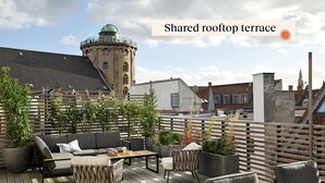 A shared rooftop terrace with outdoor seating, potted plants, and a view of the cityscape. - Attic Studio Apartment for 2 (København)