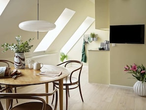 A modern dining area with a round table, chairs, a vase with flowers, and a television mounted on the wall.