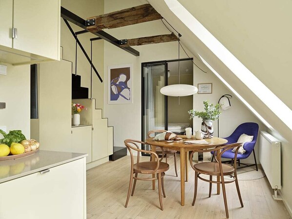 A modern kitchen with a dining area, wooden chairs, a table, and a blue chair. - One-Bedroom Attic Apartment for 4 (København)