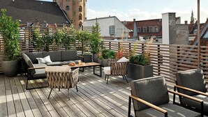 Una terraza compartida en la azotea con mobiliario exterior, plantas en macetas y vistas a la ciudad.
