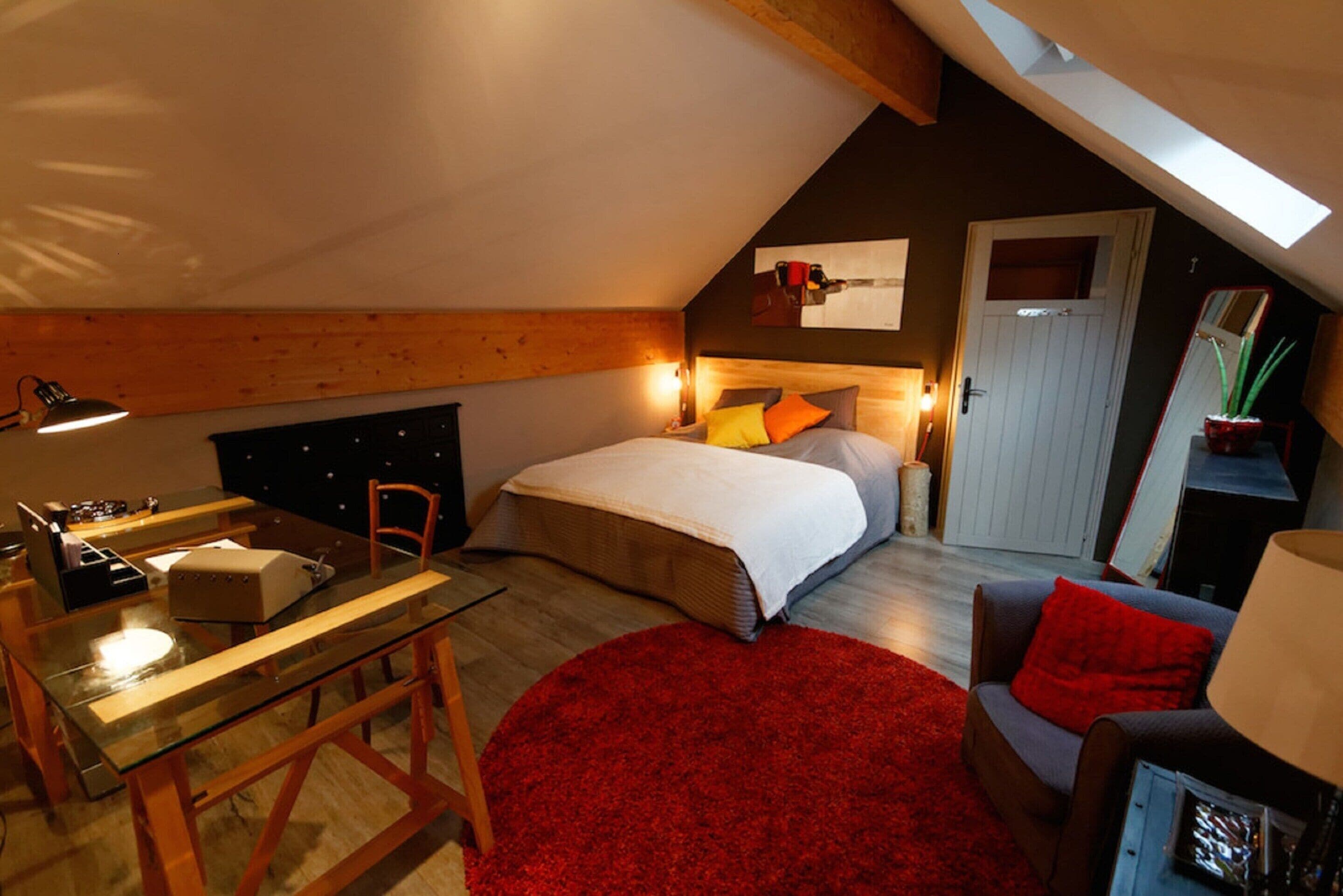 Een slaapkamer met een bed, een bureau, een stoel, een rode vloerkleed en een dakraam.
