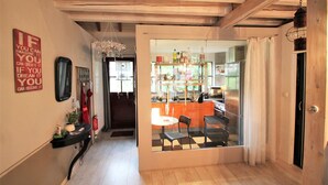 Un pasillo que conduce a un comedor con piso a cuadros, un separador de vidrio y una cocina visible a través del separador.
