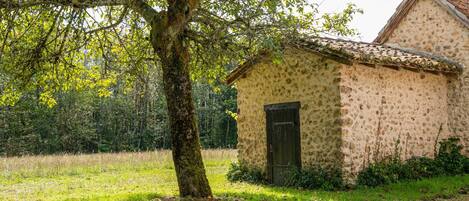 A rustic stone building with a tiled roof, surrounded by a grassy area and trees.