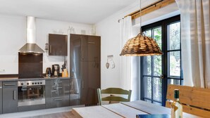 A modern kitchen with stainless steel appliances, a dining table with a book and bottle, and a large window with curtains. - Chalet in ski Area in Leogang (Leogang)