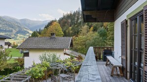 A wooden deck with a bench and a table, overlooking a garden with grapevines and a mountain backdrop. - Chalet in ski Area in Leogang (Leogang)