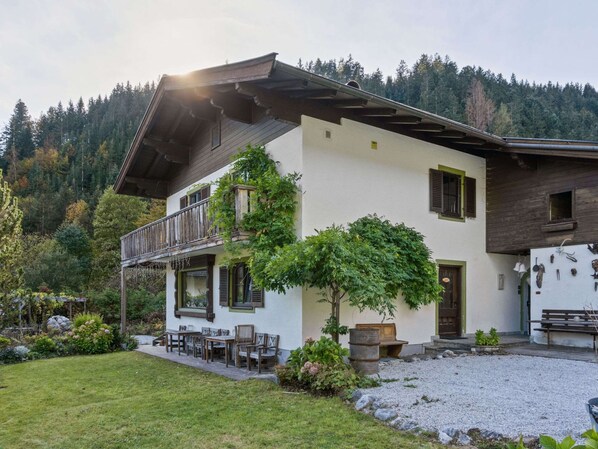 A two-story house with a balcony, a garden, and a view of a forested mountain. - Chalet in ski Area in Leogang (Leogang)