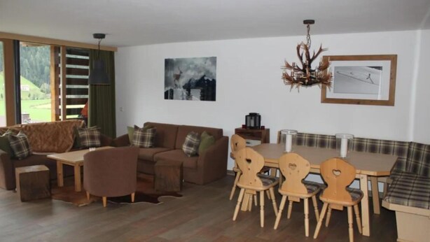 A living room with a sofa, a dining table, and chairs. There is a painting on the wall and a chandelier. - Alpine Chalet With Balcony & Sauna (Wald im Pinzgau)