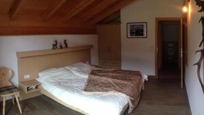 A bedroom with a bed, a chair, a wooden headboard, a shelf with figurines, and a door leading to another room. - Alpine Chalet With Balcony & Sauna (Wald im Pinzgau)