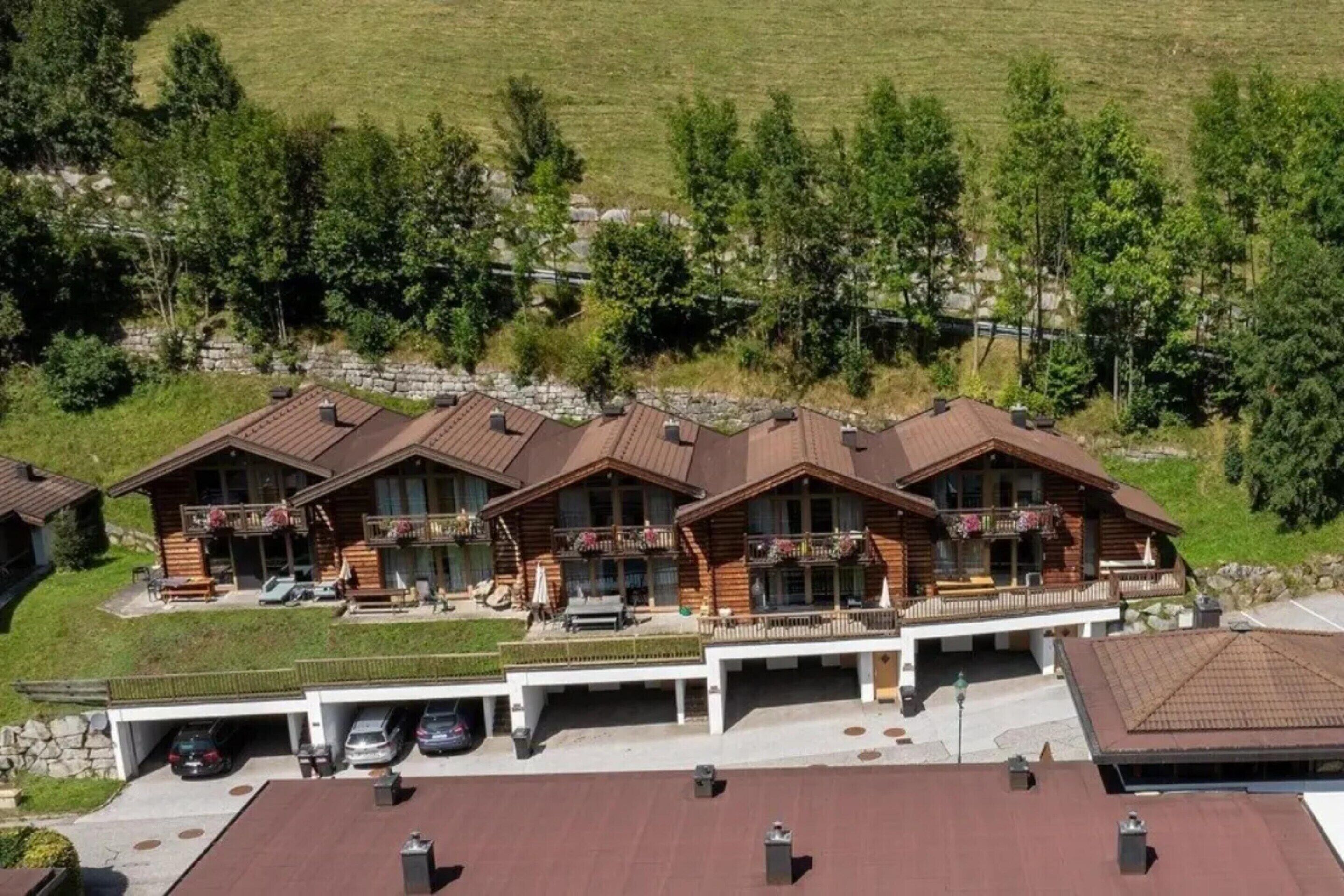 Une rangée de bâtiments de style chalet, dotés de balcons, un espace de stationnement et une colline verdoyante en arrière-plan.