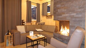 Un salon chaleureux avec une cheminée en pierre, un canapé, une table basse et une fenêtre avec des rideaux.