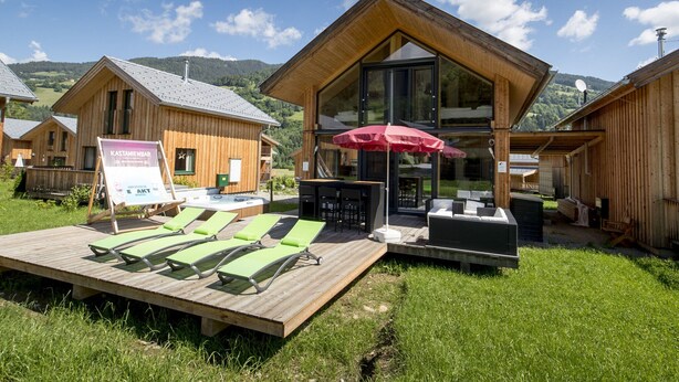 Une cabane en bois avec une extension en verre, un espace salon extérieur et un panneau indicateur.