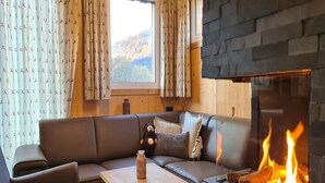 Un salon chaleureux avec une cheminée en pierre, un canapé en cuir et une vue sur l’extérieur.