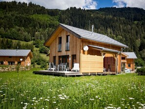 Un chalet en bois doté d’un balcon, entouré d’une prairie verdoyante et de collines boisées.