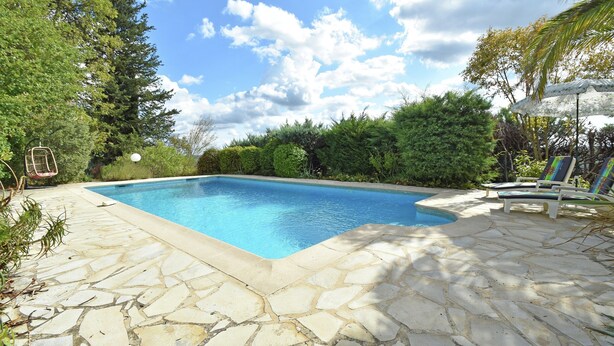 A swimming pool with stone tiles, surrounded by greenery and a clear sky. - Villa in Fayence With Provencal Charm (Fayence)