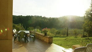 Eine Terrasse mit Tisch und Stühlen, eine Steinsäule und Blick auf eine grüne Landschaft.