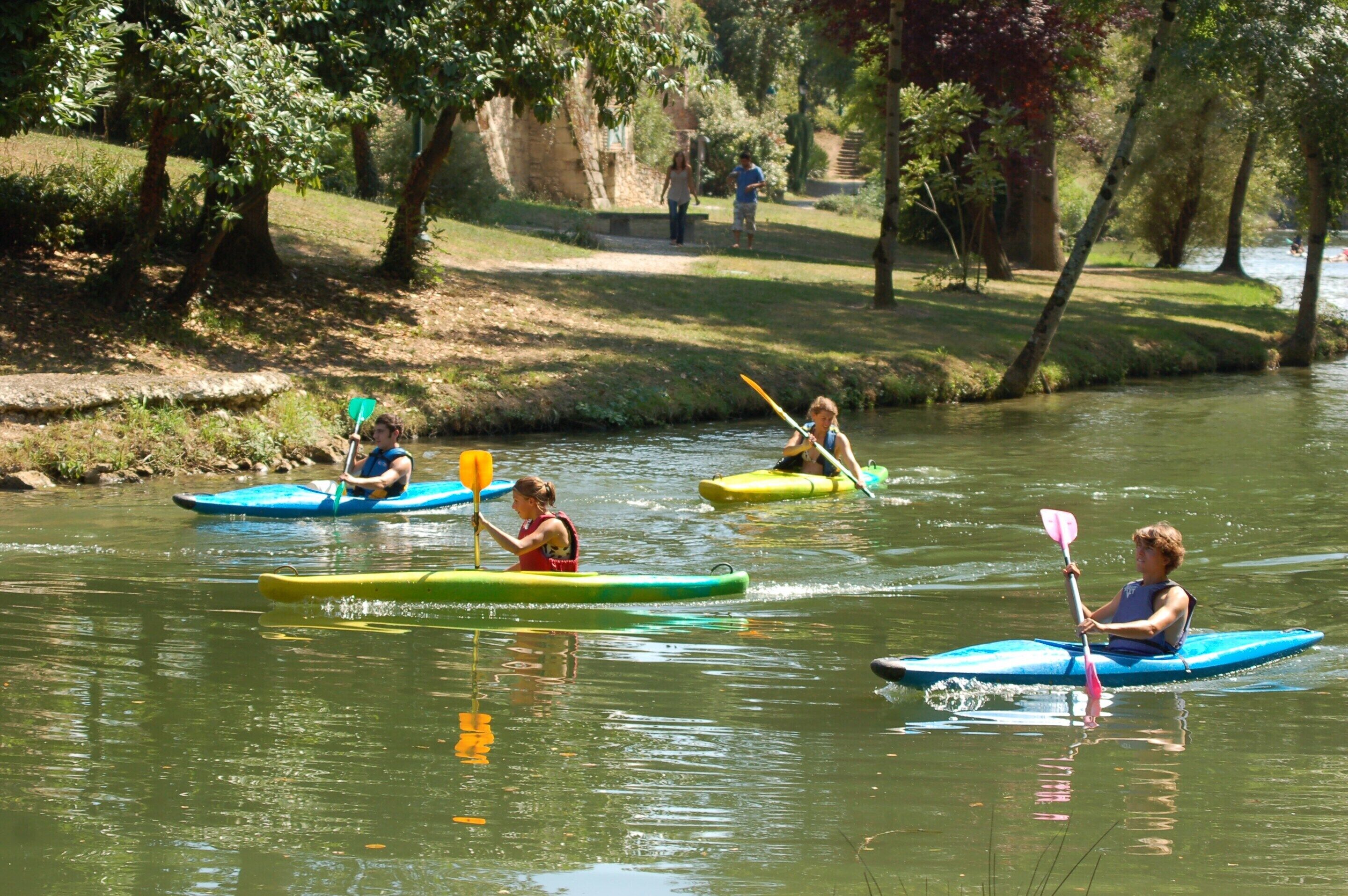 Des personnes pratiquent le kayak sur une rivière paisible, entourée d’arbres.