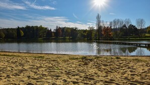 Ein sandiger Strand mit einem ruhigen See, einer Holzsteganlage und Bäumen im Hintergrund.