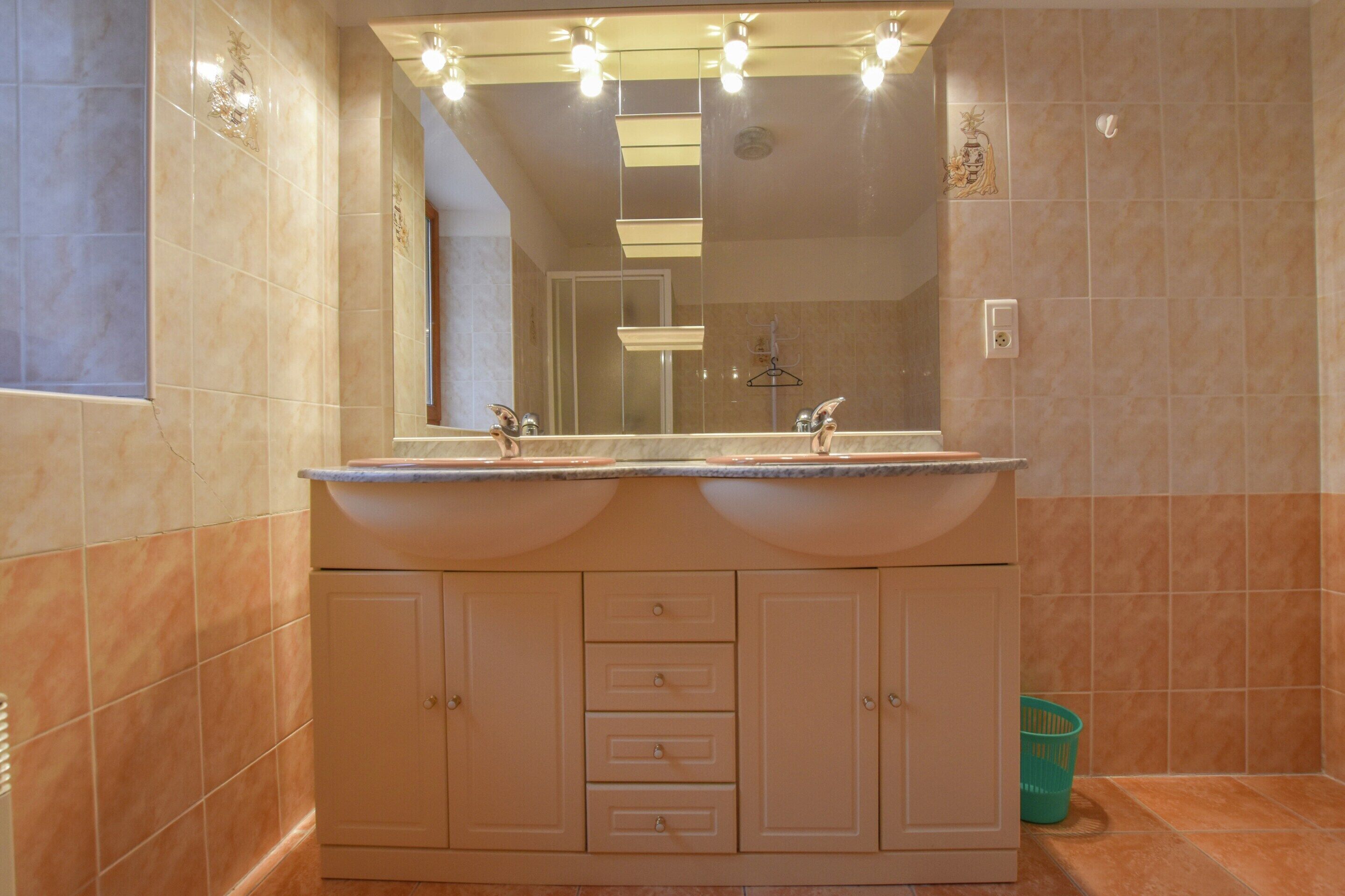 A bathroom with two sinks, a mirror with lights, and a towel rack.
