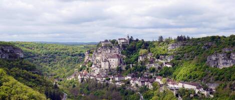 Eine historische Stadt auf einem Felsen gelegen, mit traditioneller Architektur, umgeben von üppiger Vegetation und einer gewundenen Straße.