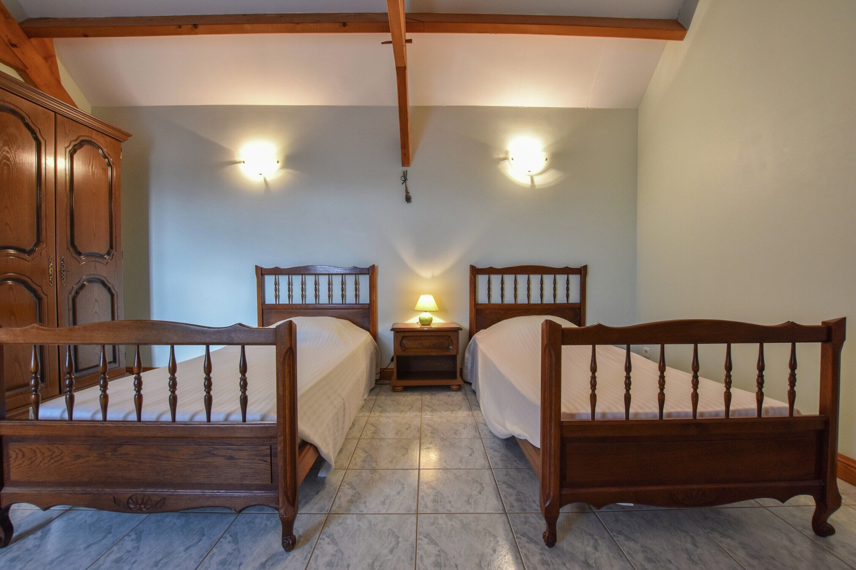 A bedroom with two wooden beds, a nightstand with a lamp, and a wooden wardrobe.