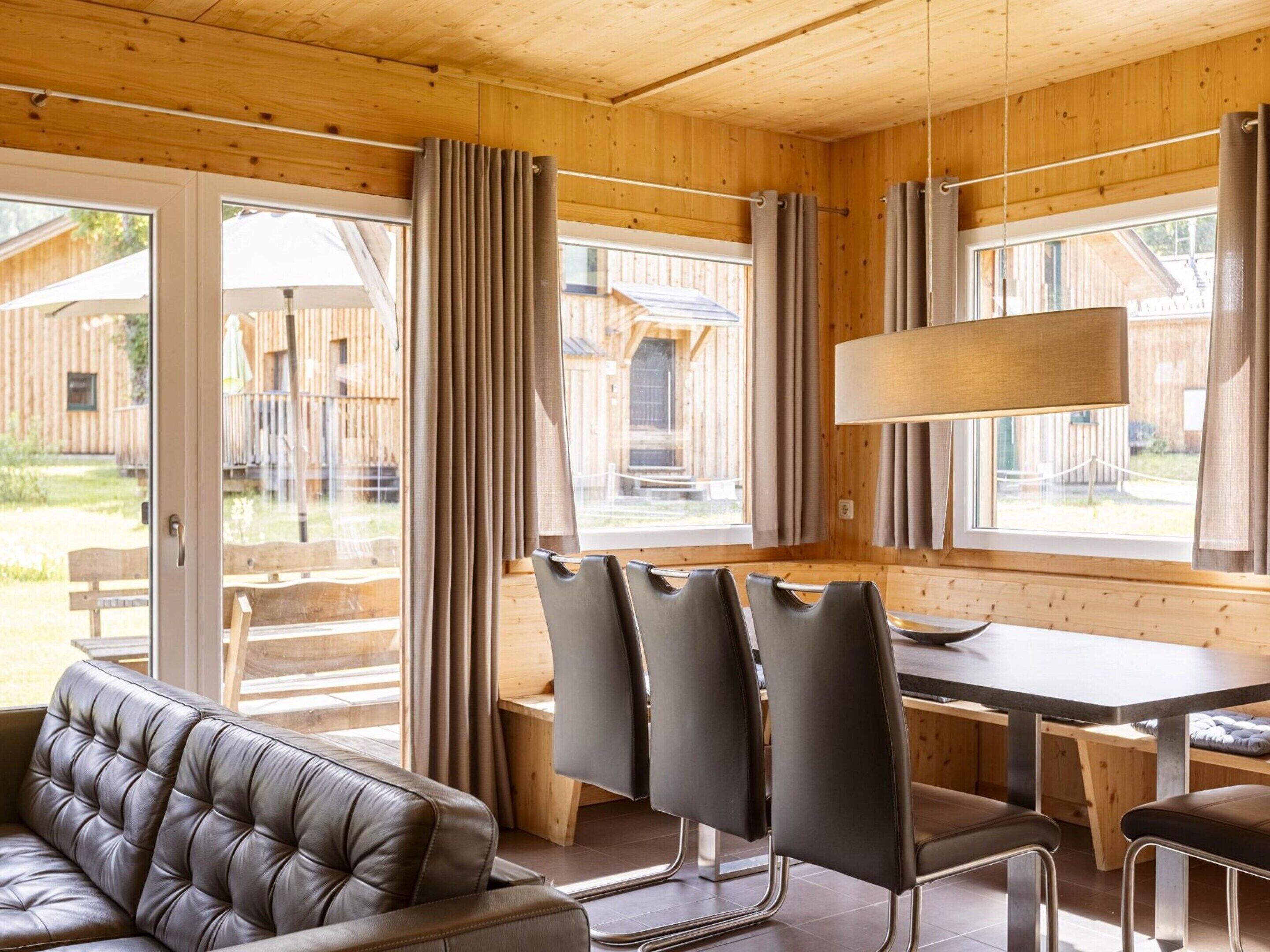 A wooden interior with a sofa, chairs, a table, and large windows.