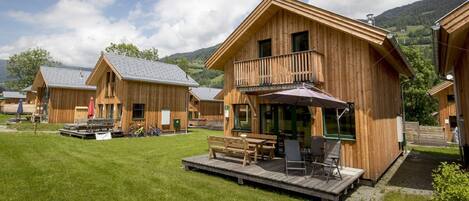 Een houten chalet met balkon, een terras met zitplaatsen en een berg op de achtergrond.
