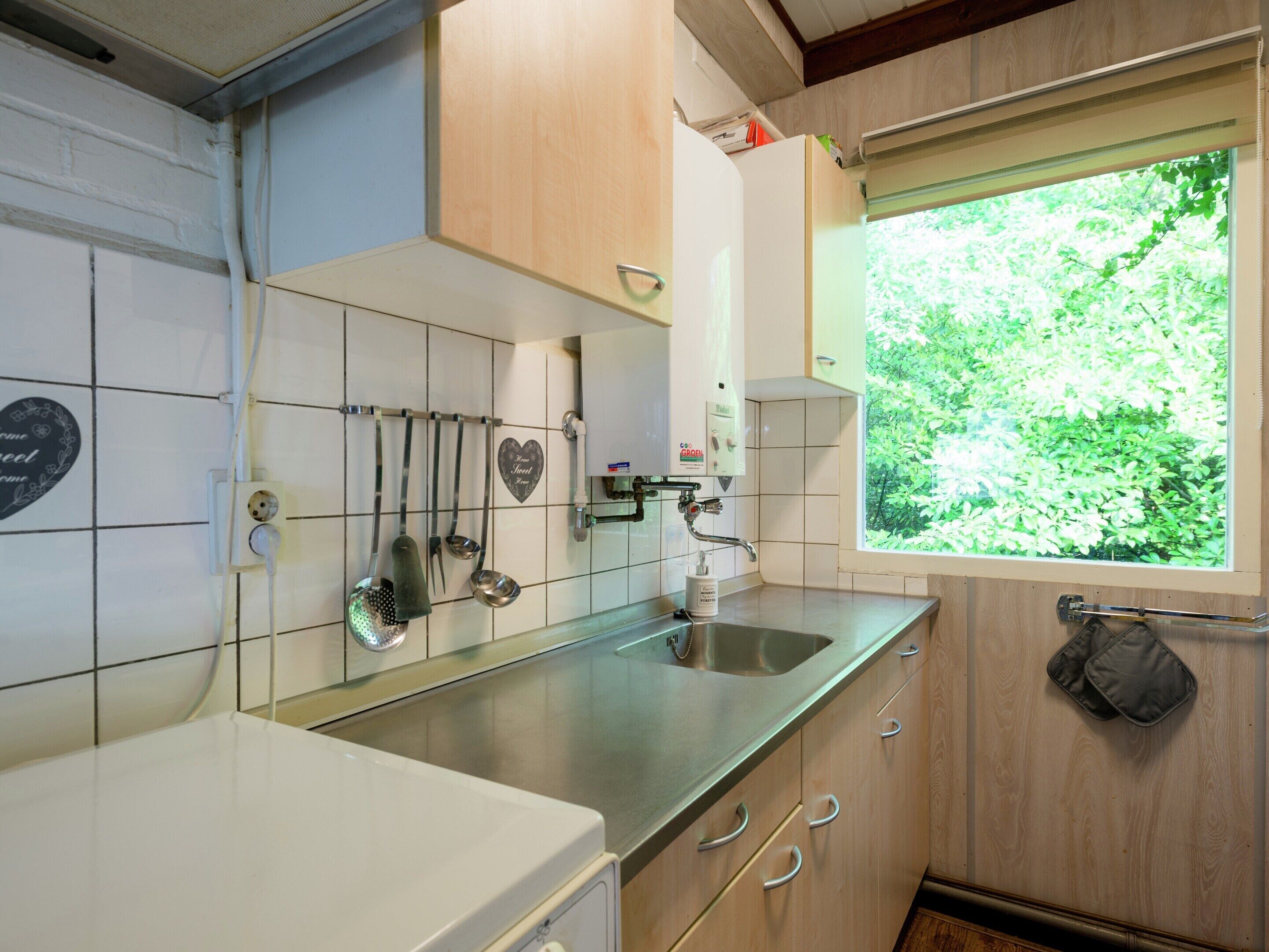 Een compacte keuken met witte kastjes, een roestvrijstalen spoelbak en een raam met uitzicht op groen.