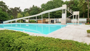A swimming pool with a slide, surrounded by greenery and a covered area with stairs. - Holiday Home in Arrien Near Beerze Nature (Arriën)