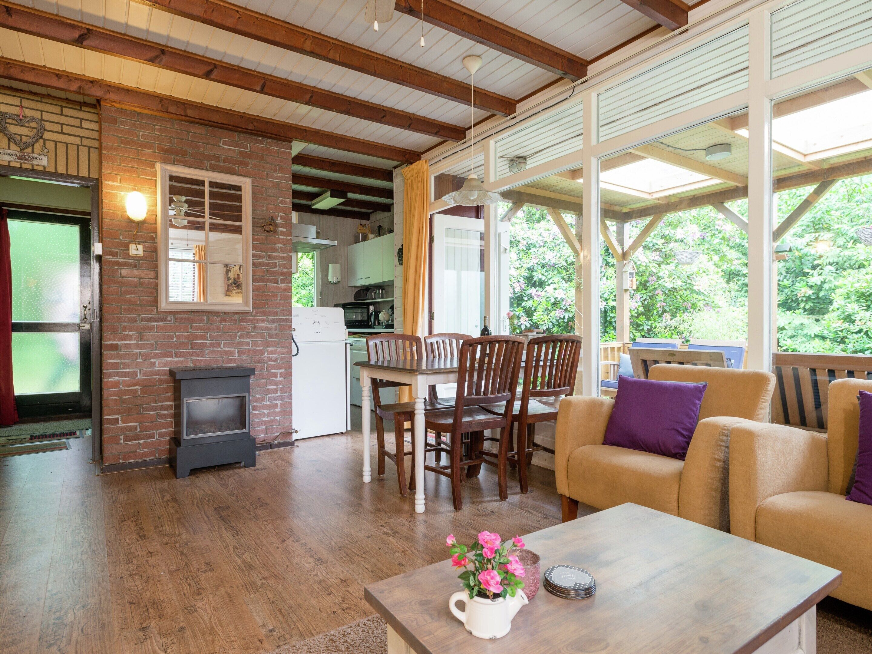 A cozy living room with a fireplace, wooden furniture, and a view of the garden through large windows.