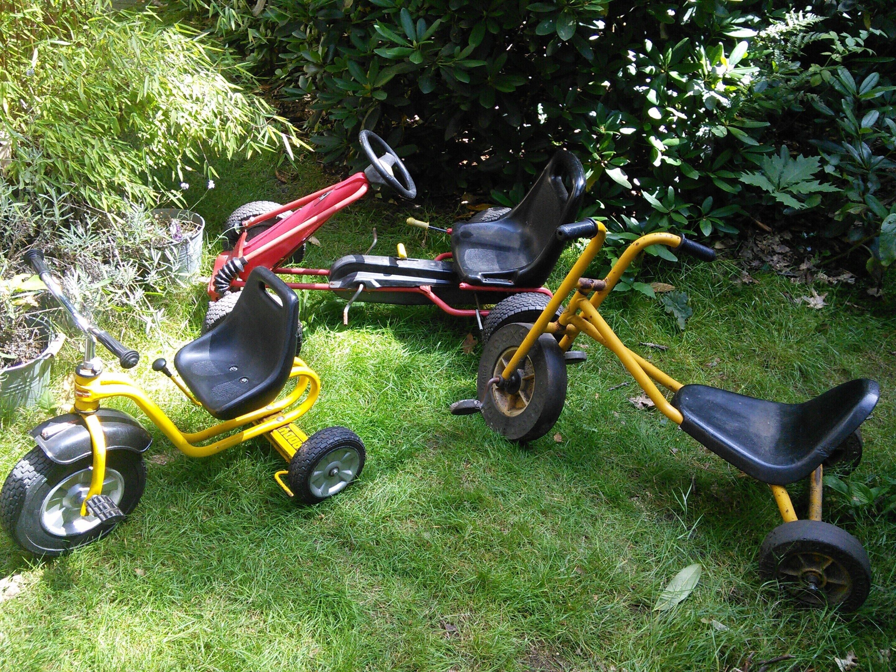 Two tricycles, one yellow and one red, parked on a grassy lawn.