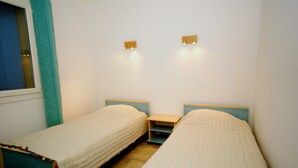 Ein Zimmer mit zwei Einzelbetten, einem kleinen Nachttisch und einem Fenster mit Vorhängen.
