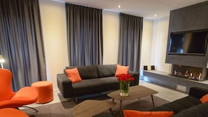 A modern living room with a sofa, ottoman, and chairs, a flat-screen TV, and a fireplace. - Villa Within National Park (De Koog)