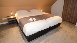 A bedroom with a bed, bedside lamps, a wooden wardrobe, and a carpeted floor. - Villa Within National Park (De Koog)