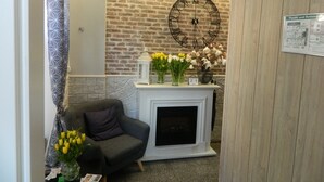 Un salón con pared de ladrillo, chimenea, un reloj y un florero con flores.