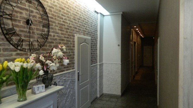 Un pasillo con pared de ladrillo, un reloj grande, una puerta y un jarrón con flores sobre una encimera.