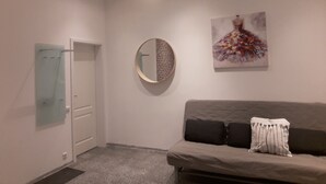 Una sala de estar moderna con un sofá gris, un espejo redondo y un cuadro colorido en la pared.