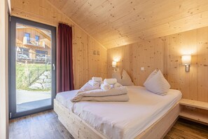 Une pièce en bois avec un lit, deux lampes fixées au mur et une porte donnant sur l’extérieur.