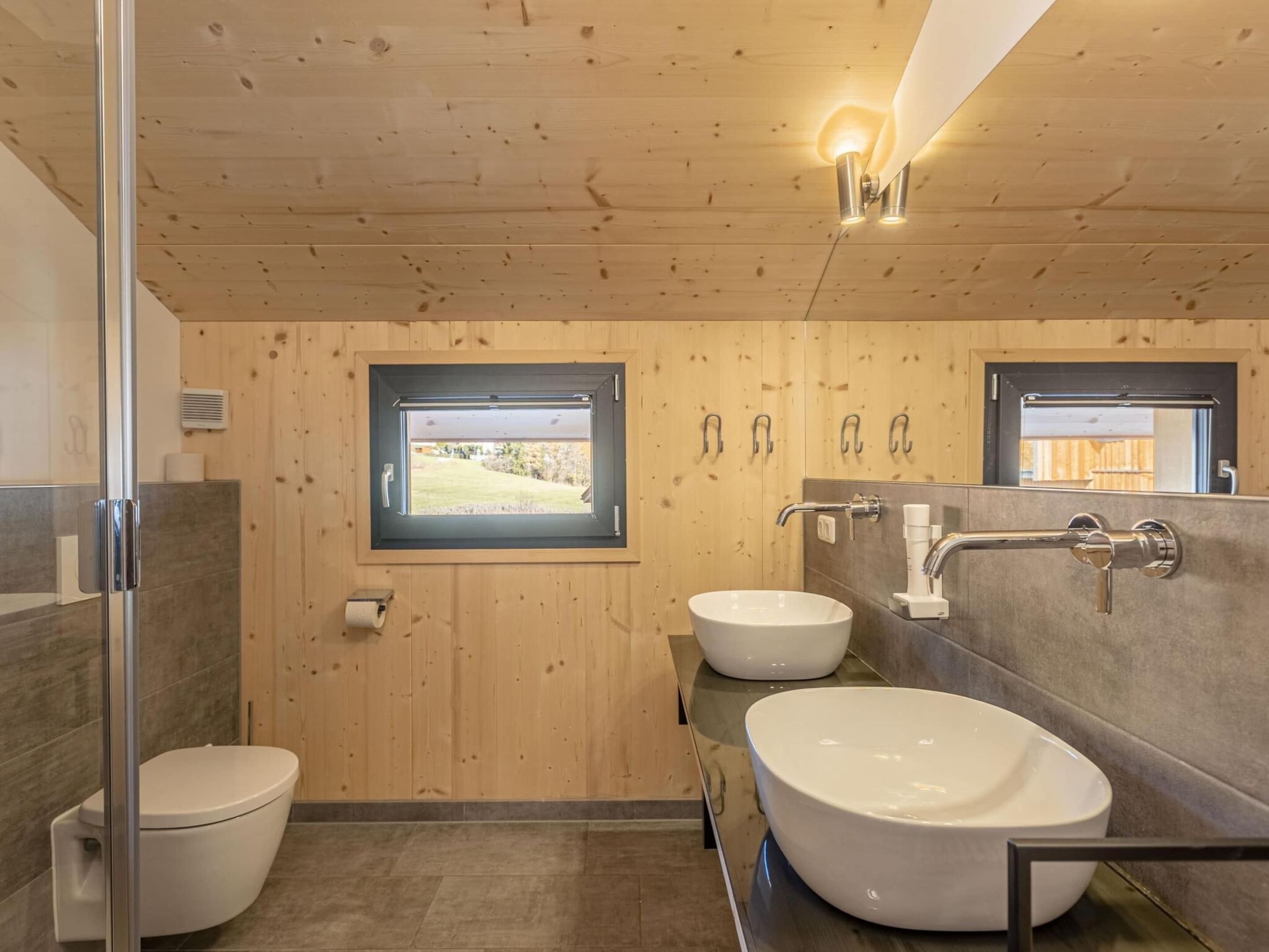 Une salle de bain moderne avec des murs en bois, deux lavabos, des toilettes et une fenêtre.