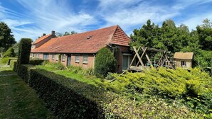 A traditional brick house with a red-tiled roof, surrounded by well-maintained hedges and greenery.