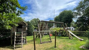 A playground with a wooden climbing structure, a slide, and a swing set.