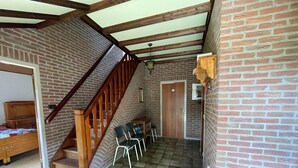 A room with a brick wall, a wooden staircase, a door, and a small table with chairs.