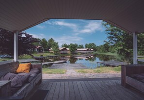 A covered outdoor seating area with wooden benches and a view of a lake and buildings in the background.
