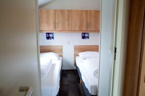 A narrow room with two beds, wooden cabinets above, and a small wall decoration.