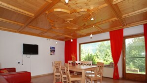 Un coin repas avec une table et des chaises en bois, un canapé rouge, un téléviseur fixé au mur et une fenêtre ornée de rideaux rouges.